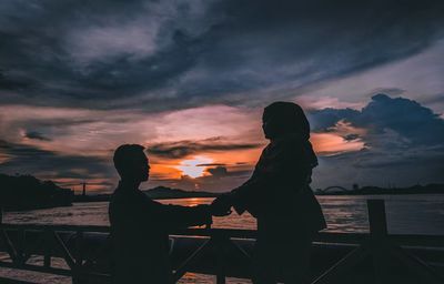 Silhouette people standing by sea against sky during sunset