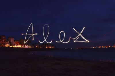 Light trails on beach against sky at night