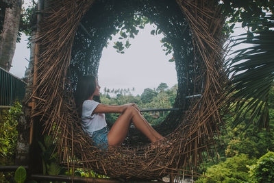 Full length side view of young woman sitting on wooden hammock