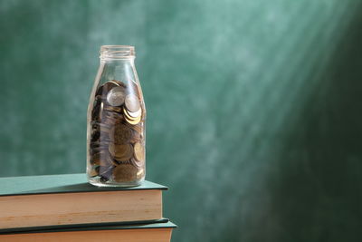 Close-up of coins in glass bottle on books against blackboard in classroom