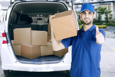 Portrait of smiling man with cardboard box gesturing by car on street