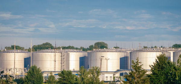 Fuel storage tanks view, oil refinery plant in morning daylight against green summer trees blue sky