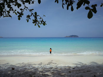 Child wearing life jacket standing on beach against sky