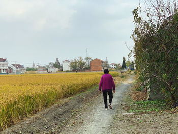 Rear view of woman walking on field against sky