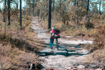 Rear view of woman walking with bicycle on dirt road