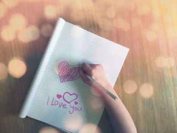 Cropped image of child drawing heart shape on book at table