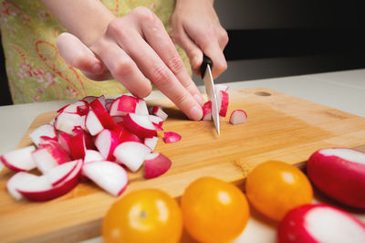 Close-up female hands of a young girl cut a fresh radish with a kitchen knife. preparing vegetable