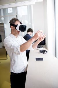 Engineer examining virtual reality simulator while coworker using computer at table