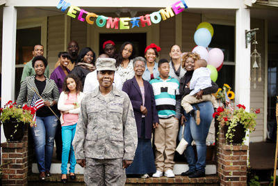 Portrait of soldier standing against family outside house