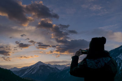 Rear view of woman photographing mountain on smart phone against sky