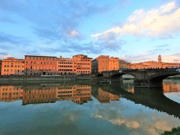 Arch bridge over river by buildings against sky