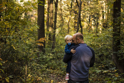 Father carrying son while standing in forest