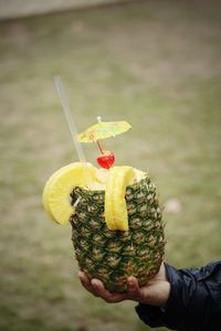 Cropped hand holding tropical cocktail in pineapple