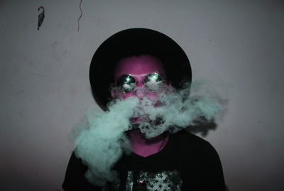 Man emitting smoke standing against wall