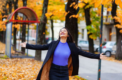 Woman in autumn. scenery with warm light and falling leaves. she turns with open arms.