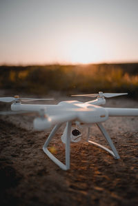 Close-up of quadcopter on field against sky during sunset