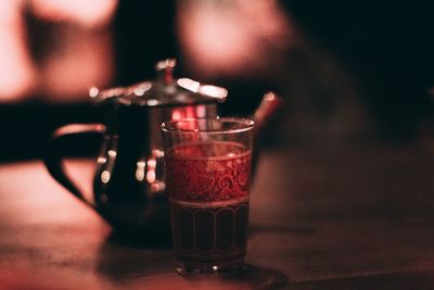 Close-up of drinking glass and kettle on illuminated table