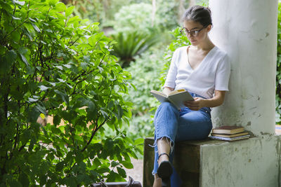 Woman reading book sitting by column outdoors