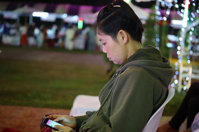 Side view of woman using smart phone while sitting on chair at night