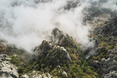 Drone view of picturesque landscape of rocky mountains with green slopes covered by thick white clouds in sunny autumn day