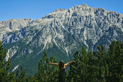 Rear view of woman with arms outstretched standing against mountain