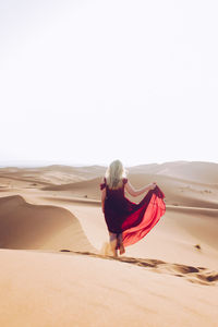 Young woman wearing red dress while walking at desert against clear sky