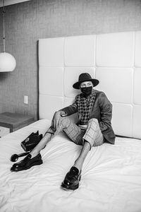 Young man sitting on bed against wall at home