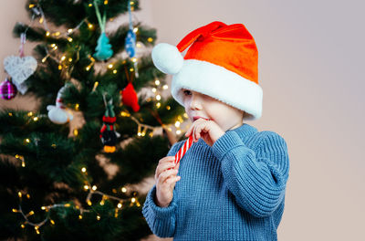 Little girl in eyeglasses and santa hat eating candy cane lollipop lo at christmas time