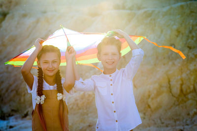 A boy and girl are hiding from the rays of the sun under a kite.