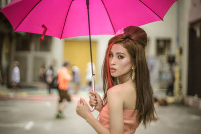 Portrait of young beautiful woman with pink umbrella standing on road