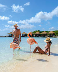 Rear view of woman sitting on beach against sky