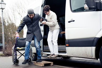 Woman assisting man while getting out from vehicle