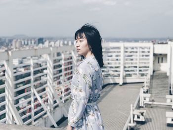 Side view of young woman standing against cityscape