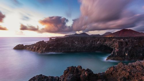 Scenic view of sea and mountains against cloudy sky during sunset