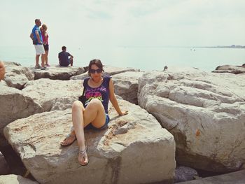 Women sitting on rock at beach against sky