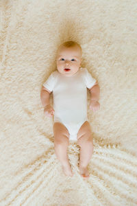 Baby in a white bodysuit lies on a light blanket on the bed