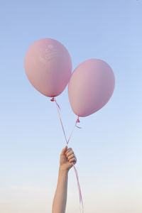 Cropped hand of woman holding balloons against clear sky
