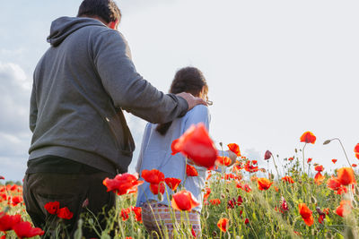 Rear view of father and daughter walking away in the poppy field on a sunny day