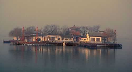 House at lake against sky during foggy weather