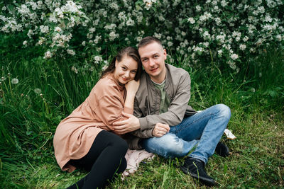 Young couple in love a girl and a man sit on the grass of a flowering apple tree 