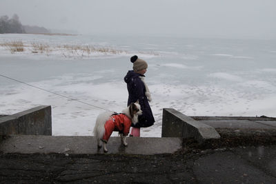 Rear view of boy playing with dog at beach