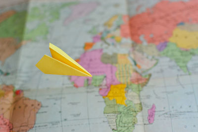 Close-up of yellow paper airplane flying over world map