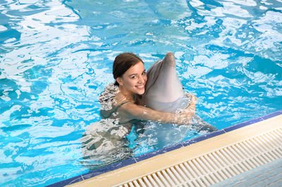 Portrait of smiling young woman with dolphin swimming in pool