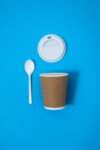 Reusable cup with plastic cap and spoon on a plain blue background