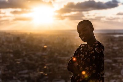 Smiling woman standing with arms crossed with city in background during sunset