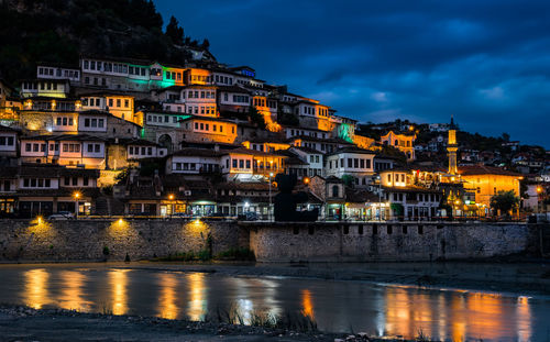 Illuminated buildings by river against sky at night