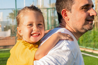 Happy father carrying daughter on back at sports ground