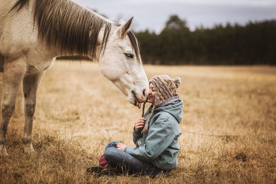 Happy horse licking young girls face in a field in the fall
