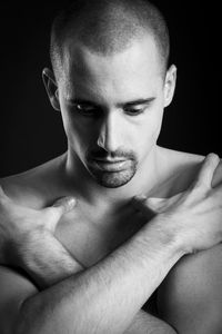 Thoughtful shirtless man covering chest with hands against black background