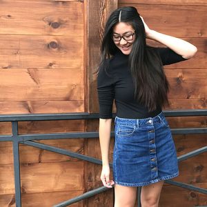 Smiling woman with hand in hair standing against wooden wall